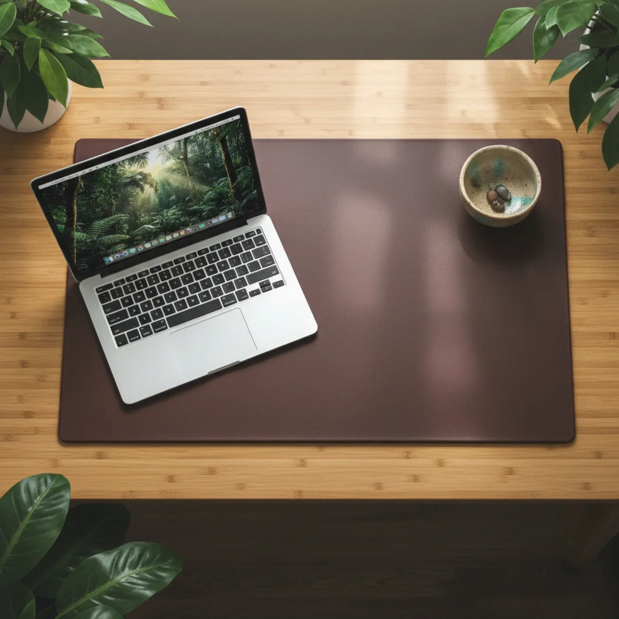 Chocolate brown leather desk mat on wooden desk with laptop and bowl, surrounded by plants