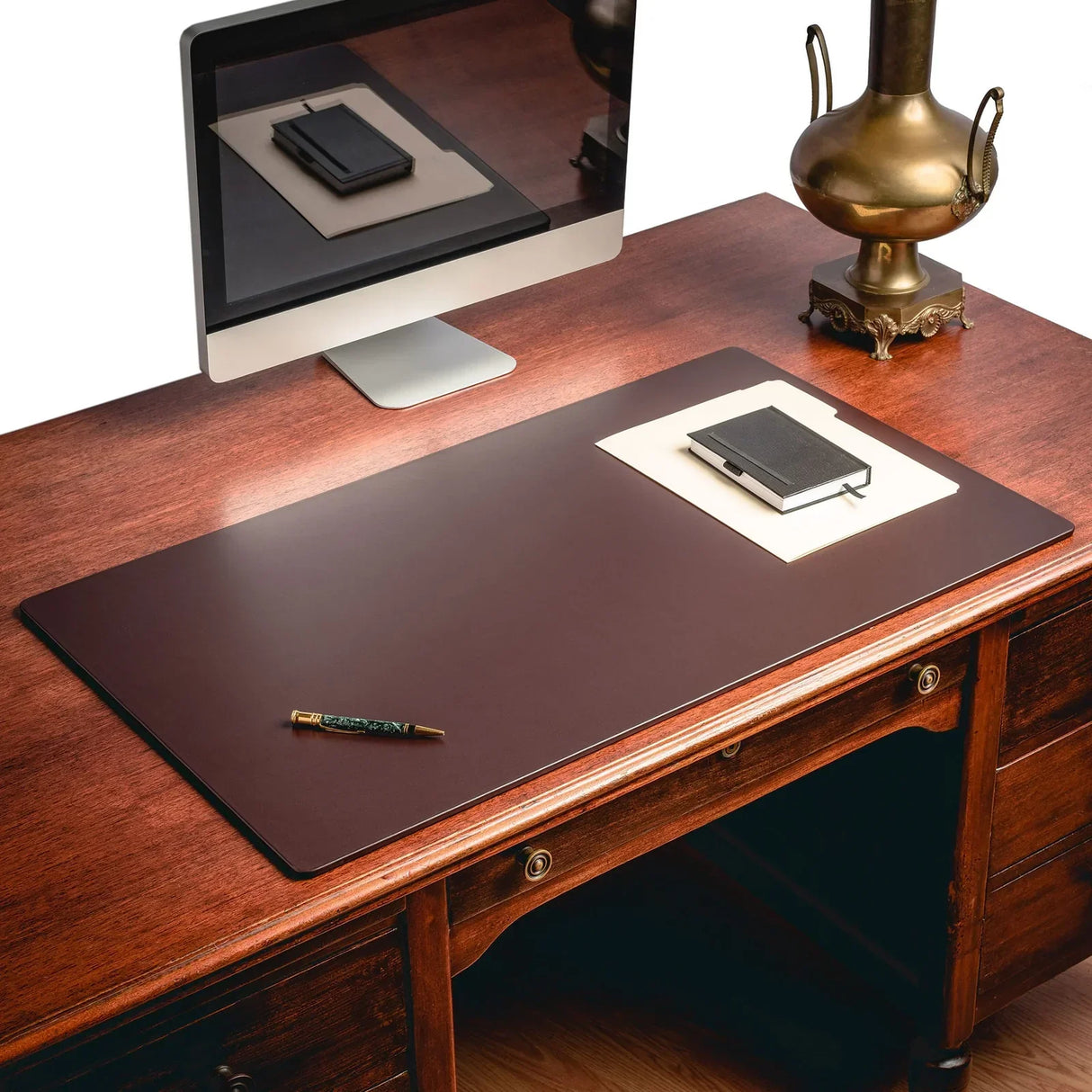 Chocolate brown leather desk mat on wooden desk near computer, lamp, and notebook