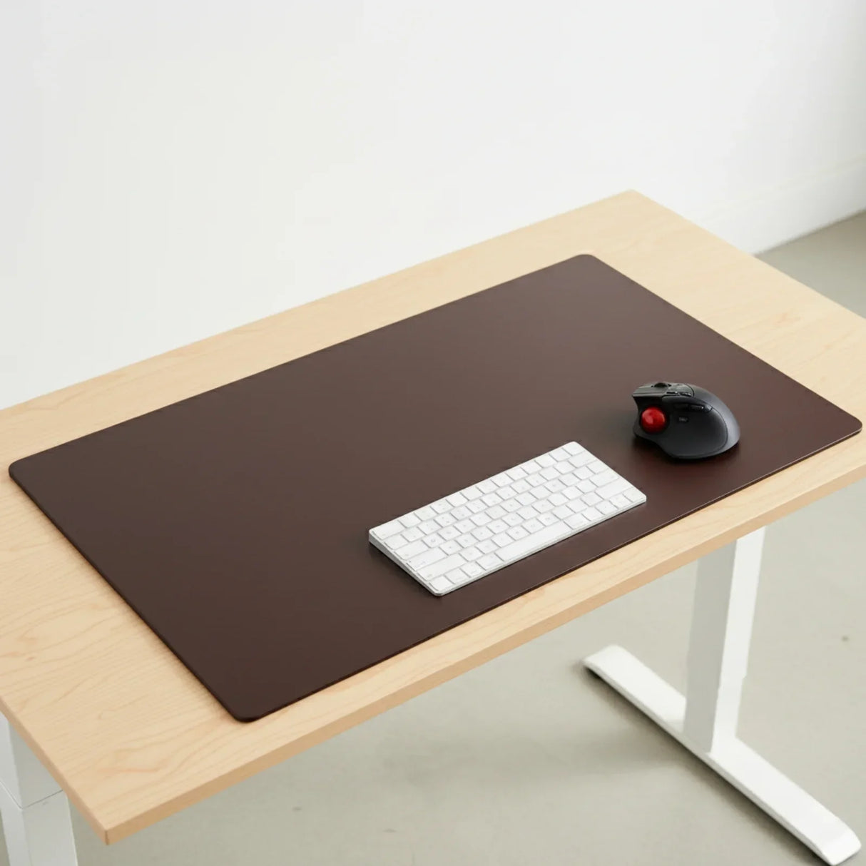 Chocolate brown leather desk mat on a light wood desk with keyboard and trackball mouse