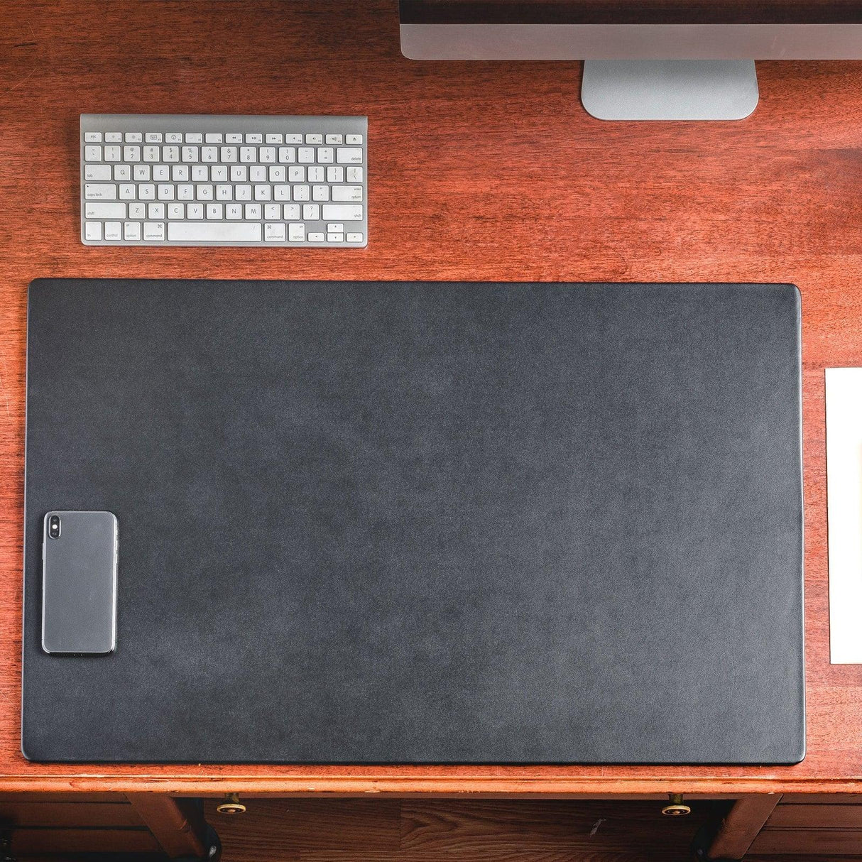 Black leather desk mat on wooden office desk with keyboard and smartphone