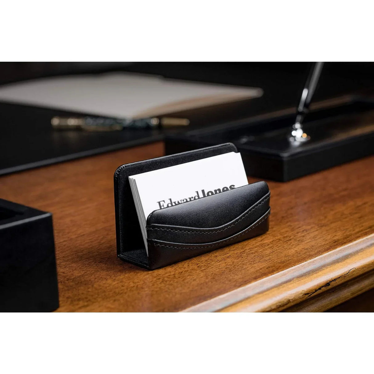 Black leather business card holder on wooden office desk with business cards inside