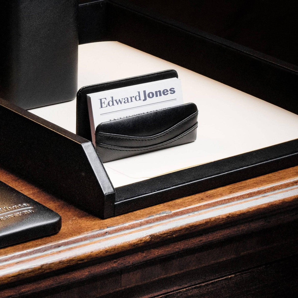 Black leather business card holder on wooden desk organizer with cards inside