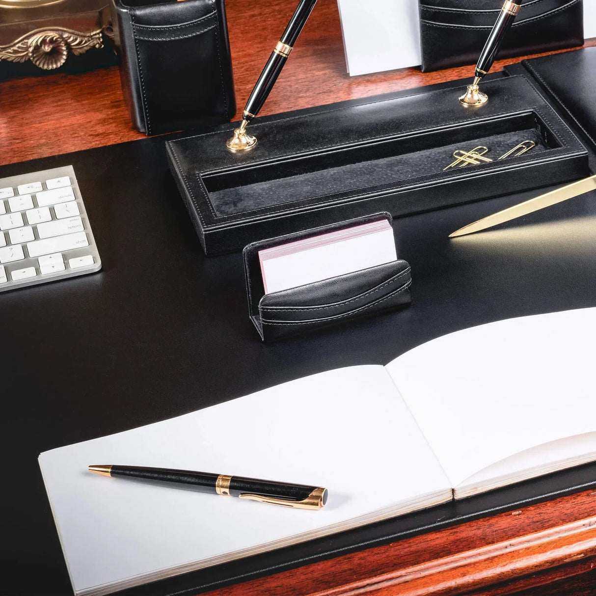 Black leather business card holder on elegant office desk with pens, notebook, and keyboard