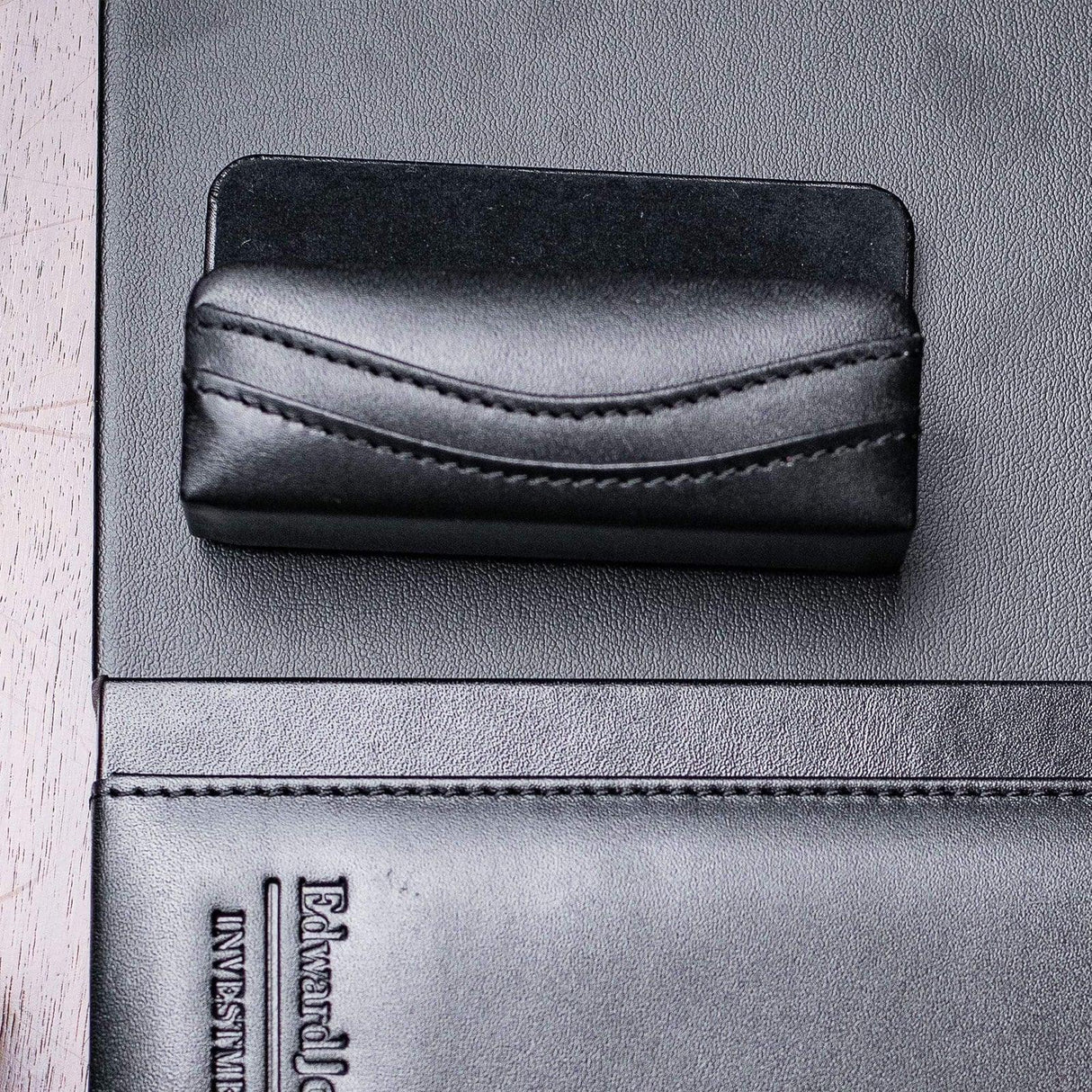 Black leather business card holder with stitched detail on dark desk organizer