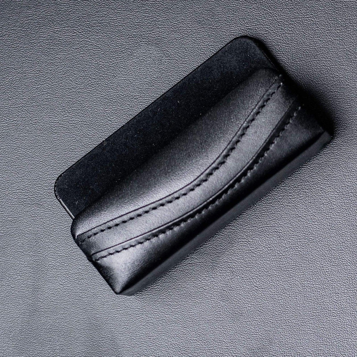 Black leather business card holder with stitched design on textured surface