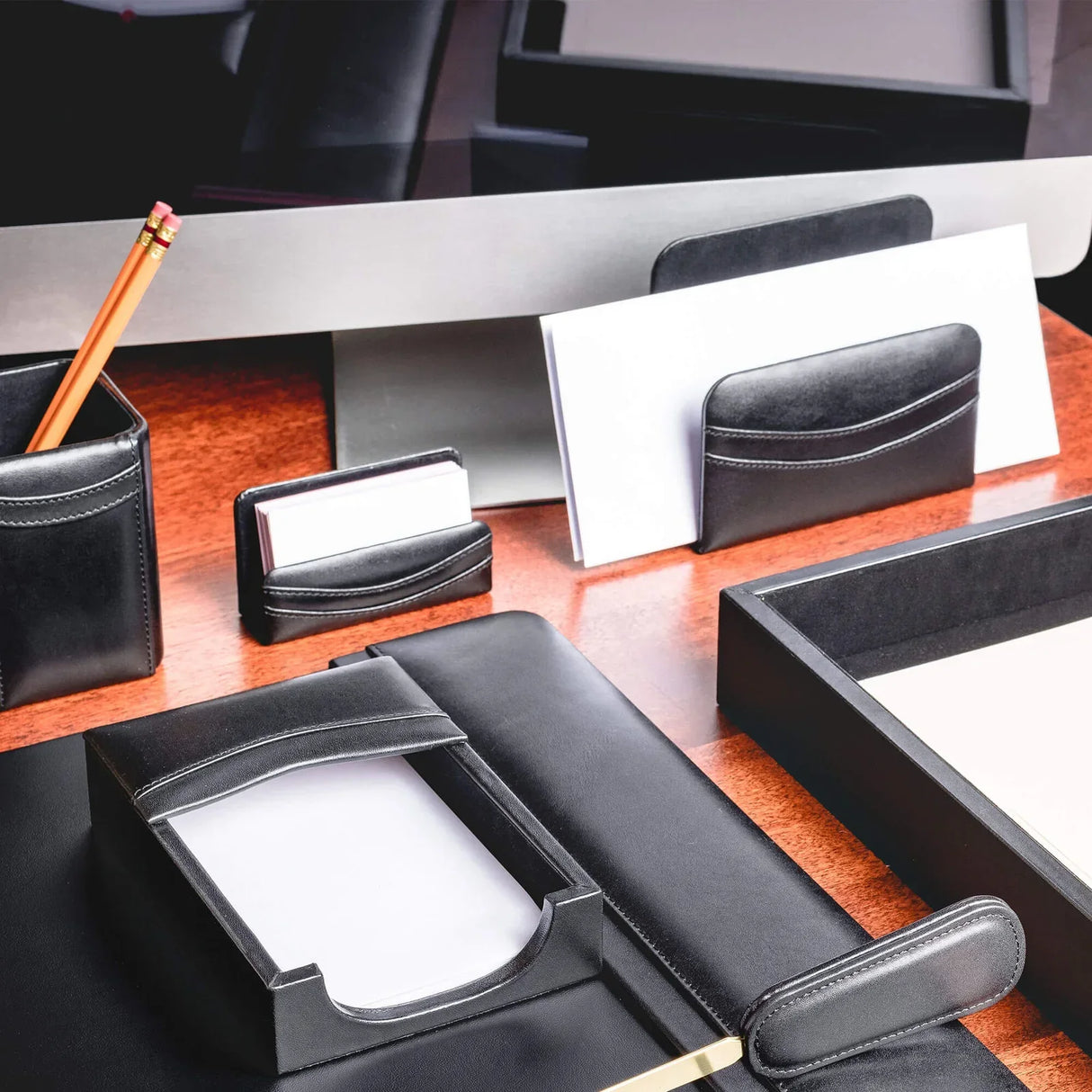 Black leather business card holder on office desk with matching desk accessories