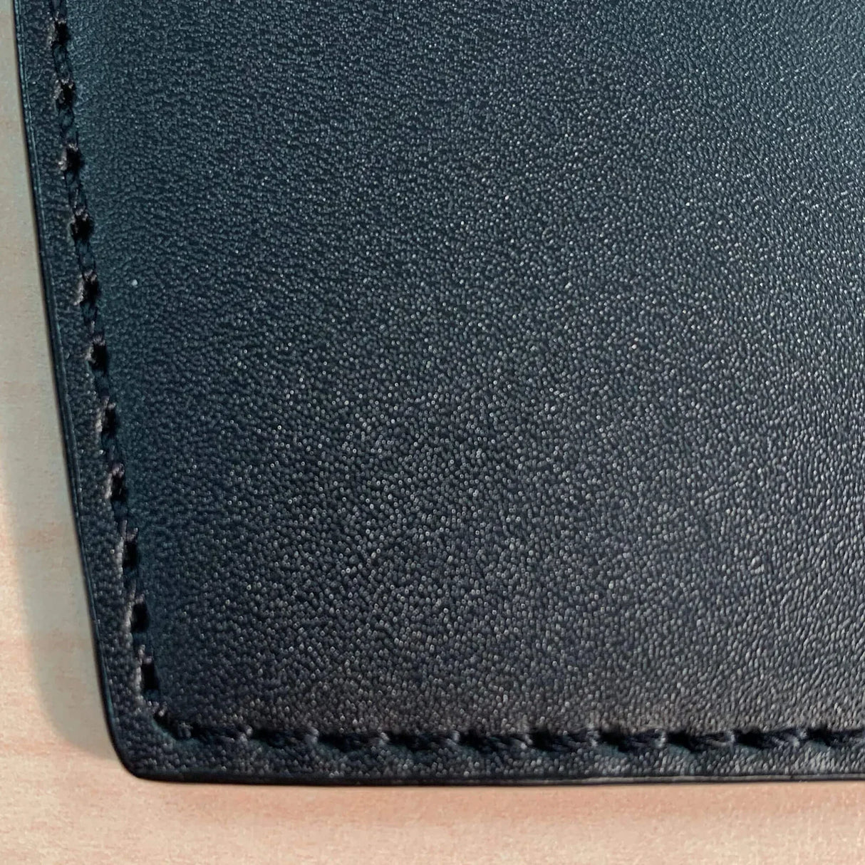 Close-up of black leather mouse pad with stitched edge on a light wood desk