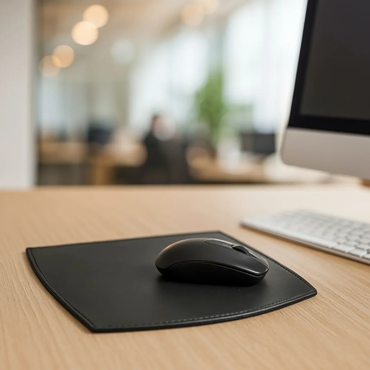 Black leather mouse pad with wireless mouse on modern office desk near computer keyboard