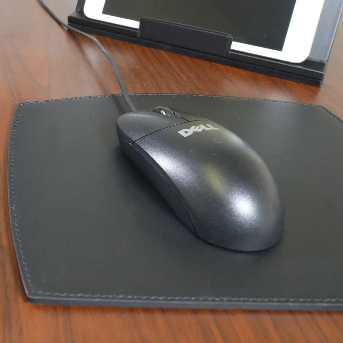 Black leather mouse pad on wooden desk with wired mouse and tablet stand