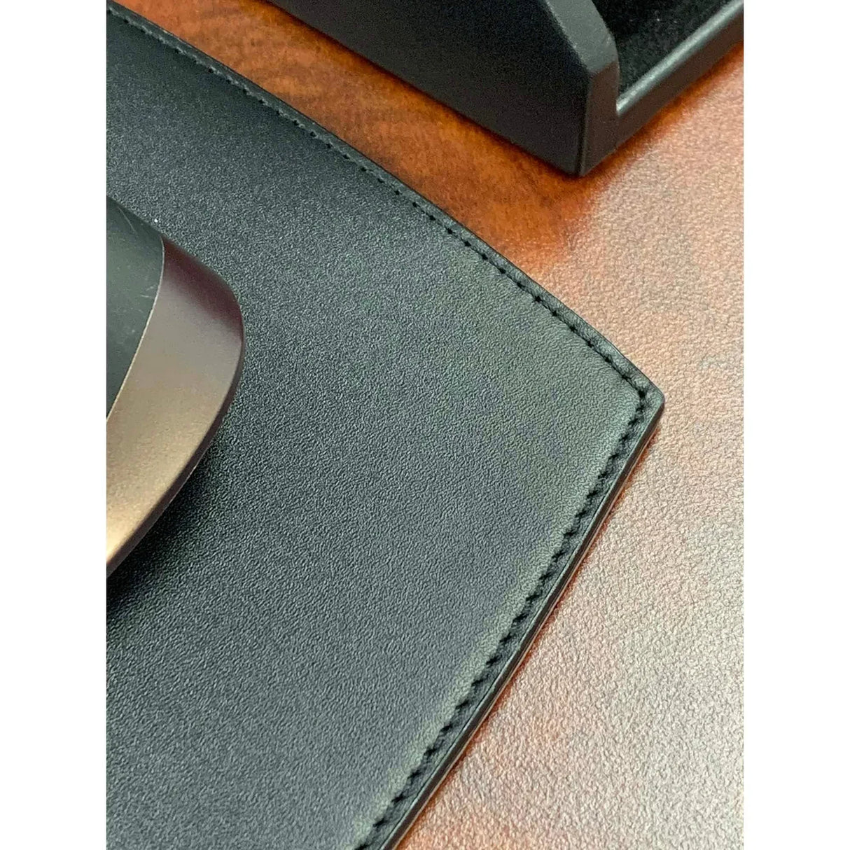 Black leather mouse pad with stitched edge on brown desk, close-up view