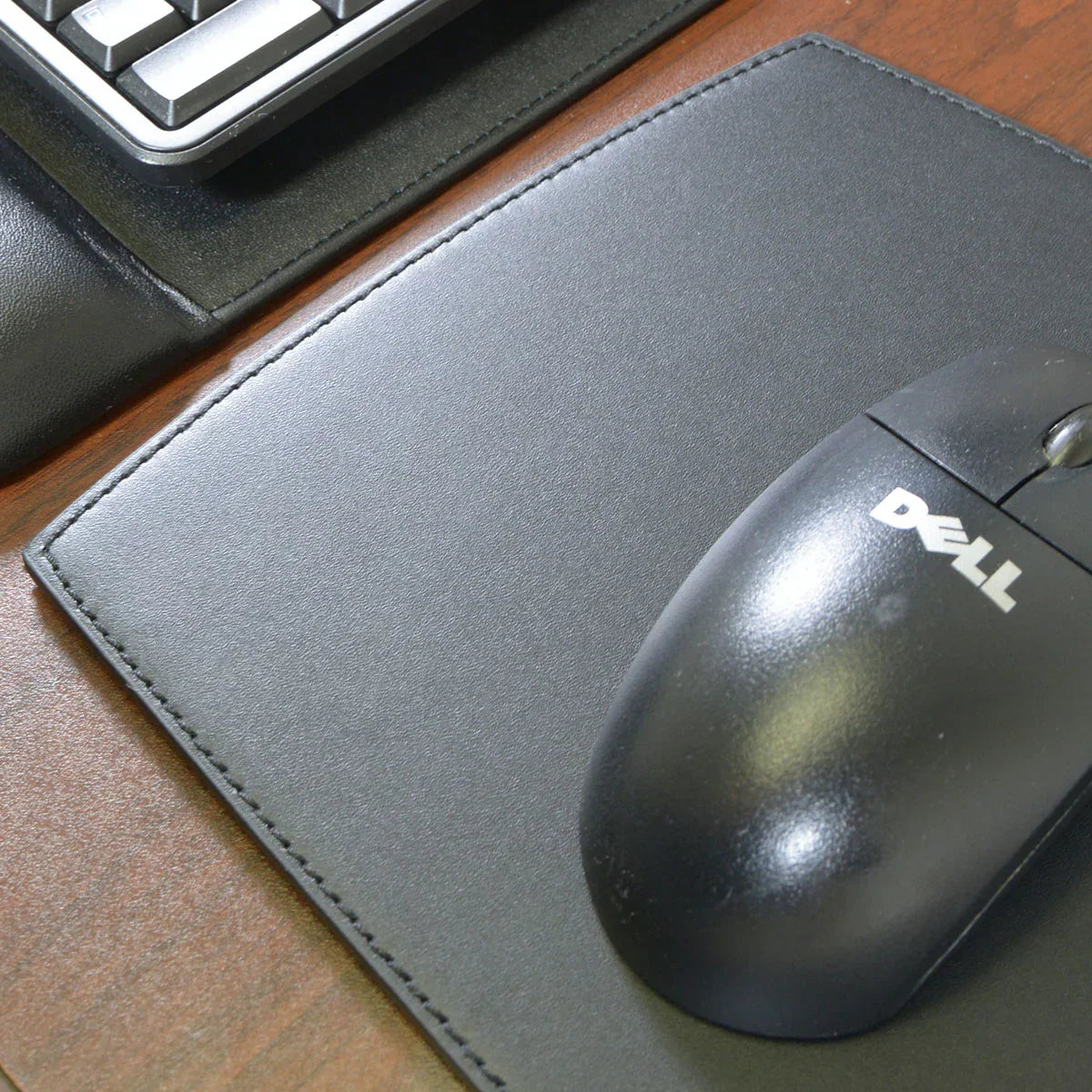 Black leather mouse pad on wooden desk with computer mouse and keyboard