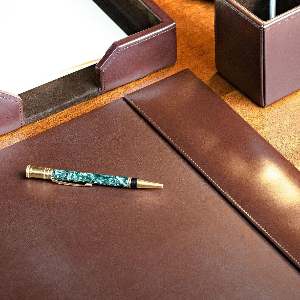 Dark brown leather desk pad with gold pen, organizer and tray on wood office desk