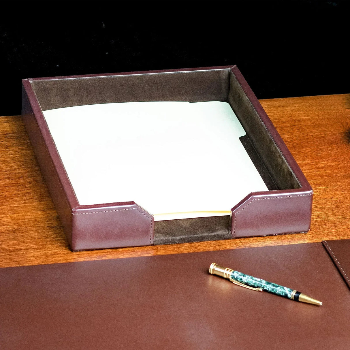 Dark brown leather letter tray with documents on a wooden office desk