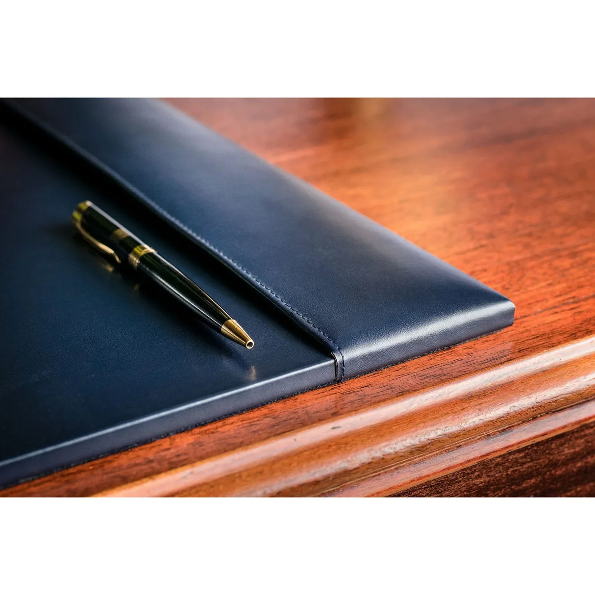 Navy blue leather desk pad with pen on wooden desk, office workspace accessory.