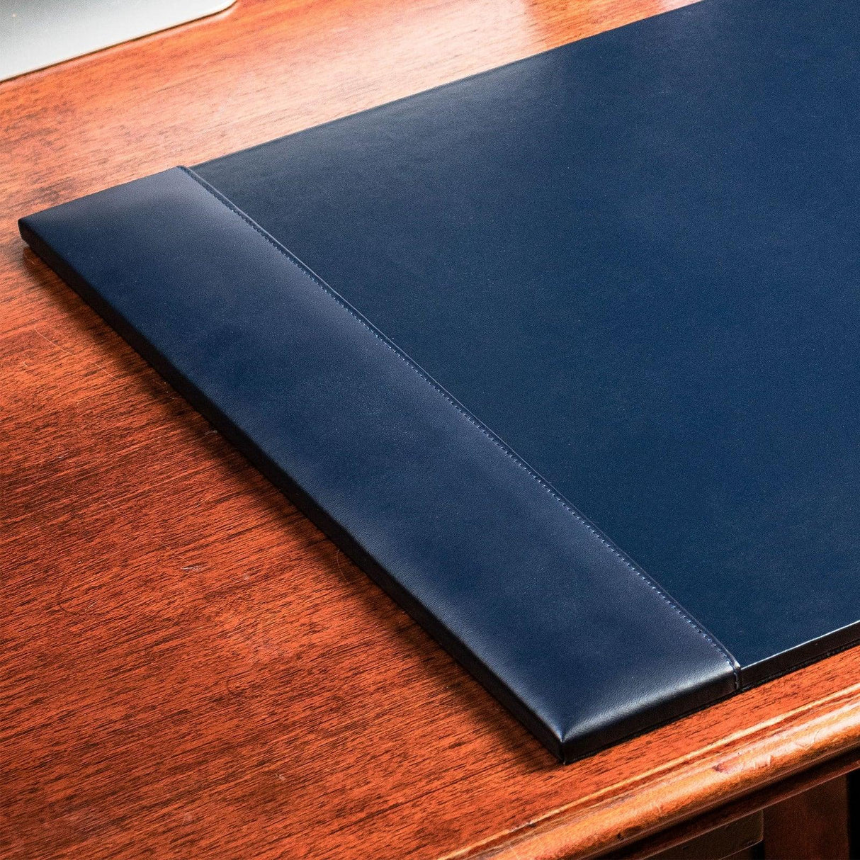 Navy blue bonded leather desk pad on a wooden office desk