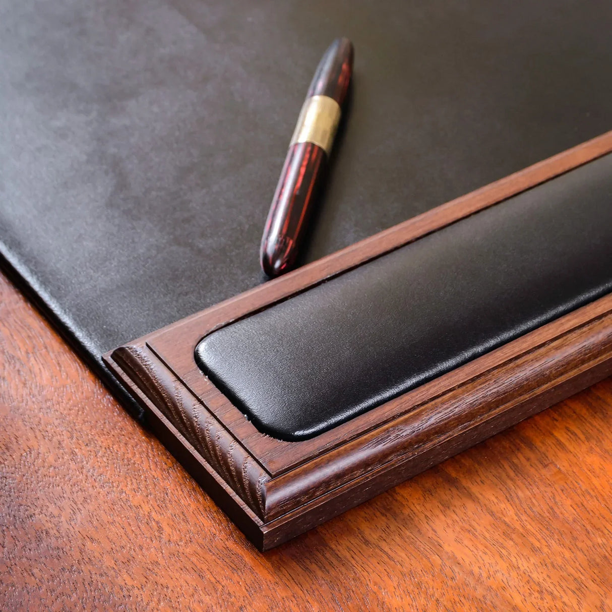 Walnut and black leather desk pad with pen on wood surface, side rail detail shown