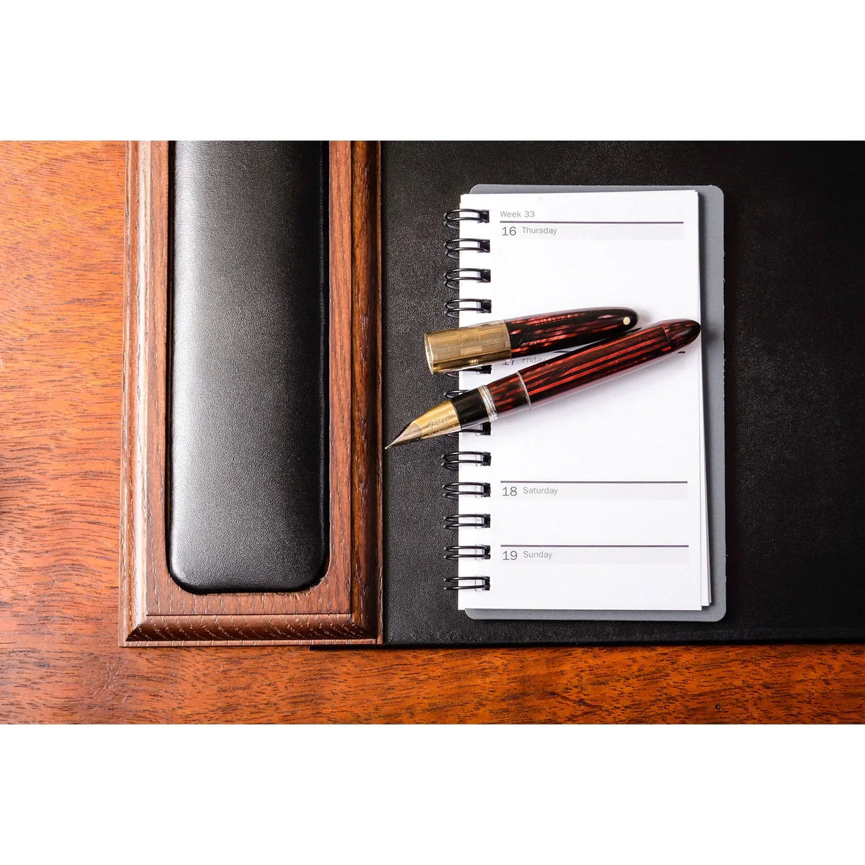 Walnut and black leather desk pad with notebook and fountain pen on wooden desk