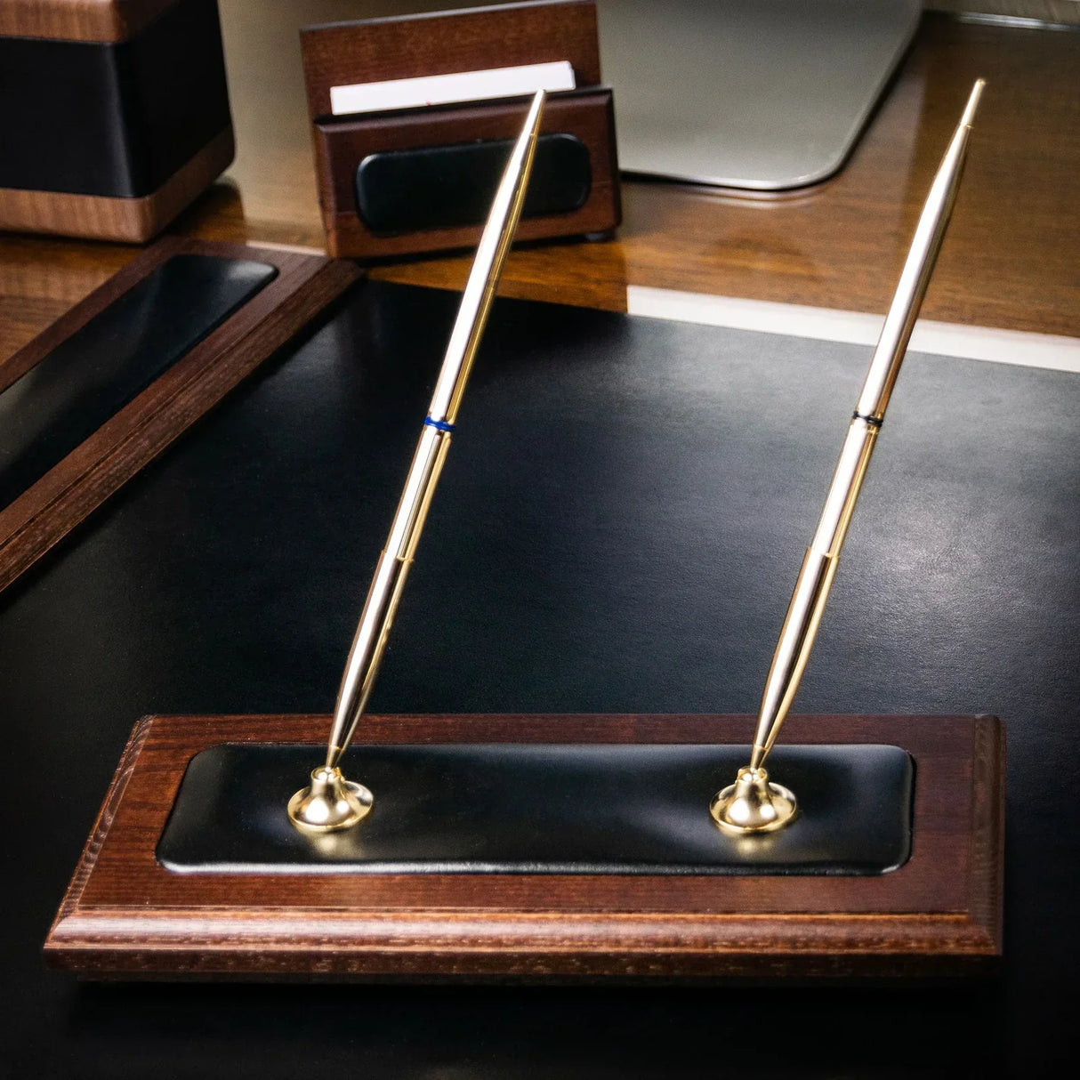 Walnut double pen stand with black leather base and two gold pens on office desk