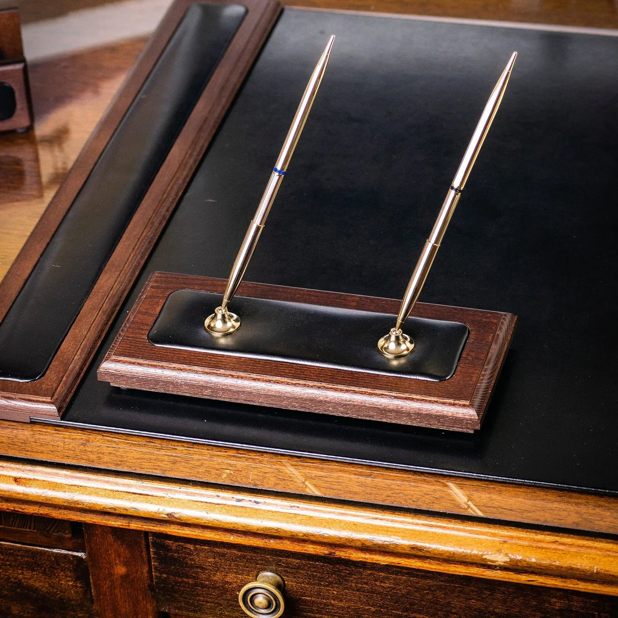 Walnut and black leather double pen stand with gold pens on a wooden office desk