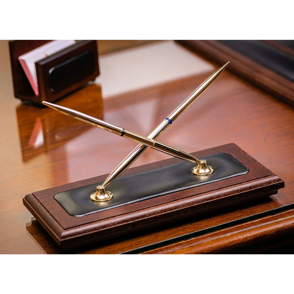 Walnut and black leather double pen stand with two gold pens on an office desk