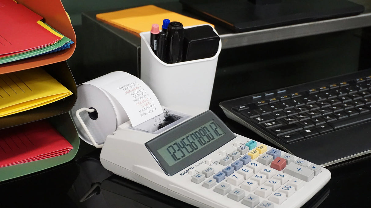 Office desk with a Sharp printing calculator, paperwork organizer, keyboard, and pen holder