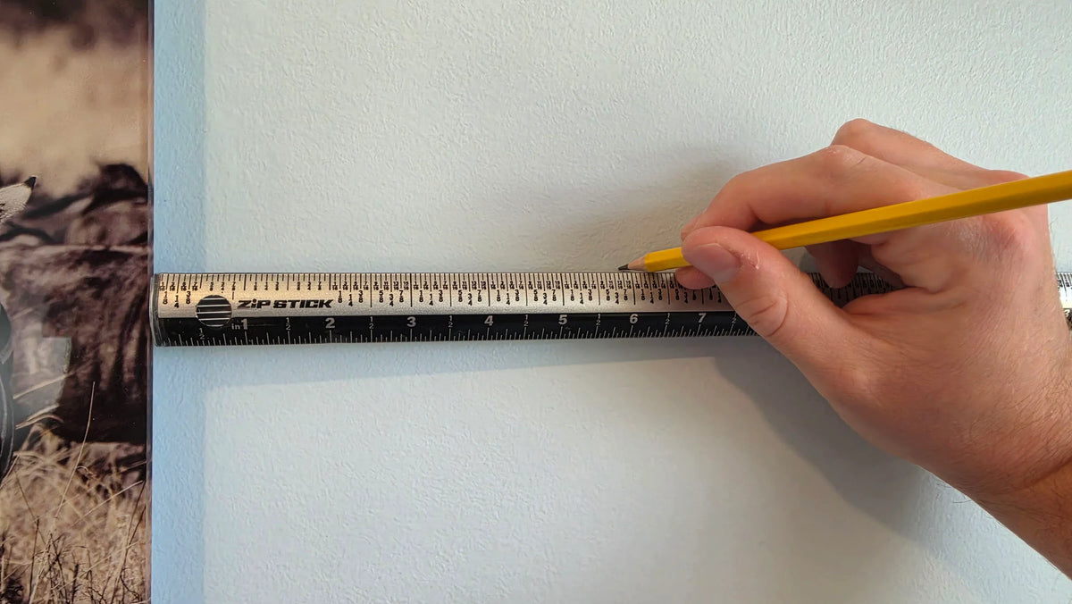 A hand using a yellow pencil to mark measurements on a Zip Stick 18 inch magnetic ruler.