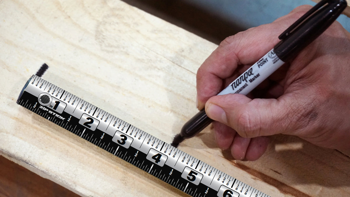Hand using a marker to mark a Victor® Zip Stick magnetic measuring tool on wood.