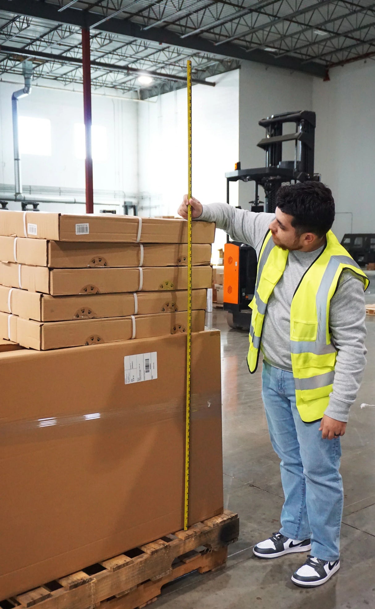Worker measuring stacked boxes in warehouse with tape measure