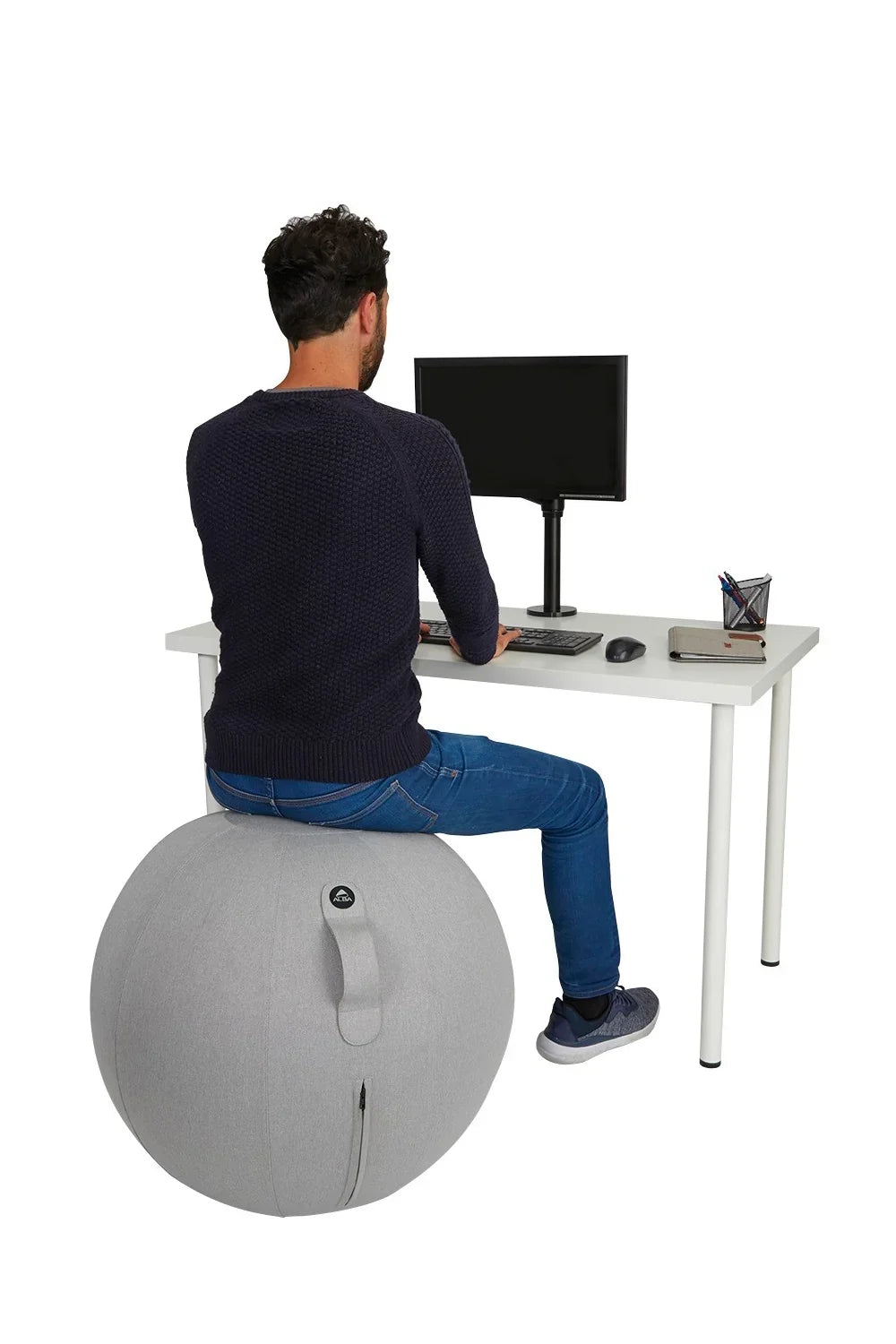 Man sitting on a grey Alba MoveHop Ergonomic Seat Ball at a white office desk.