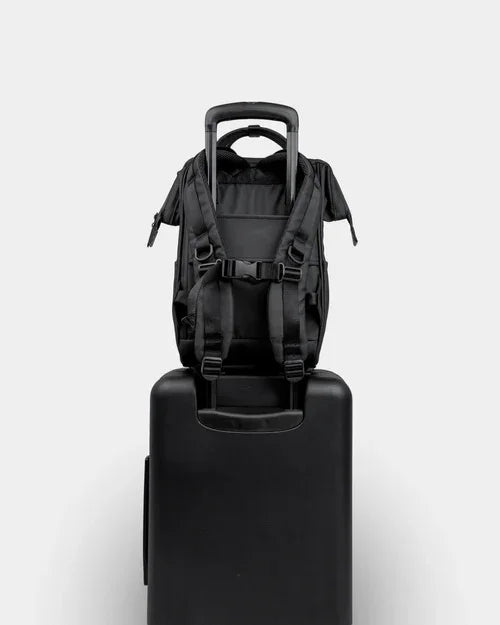 Black compact backpack with shoulder straps securely attached to suitcase handle, travel-ready.