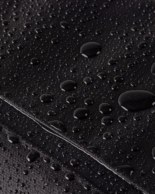 Close-up of water droplets on black waterproof surface, showcasing moisture resistance.