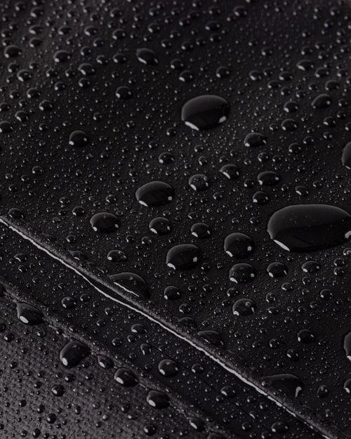 Black waterproof surface with water droplets, ideal for office or school gear protection.