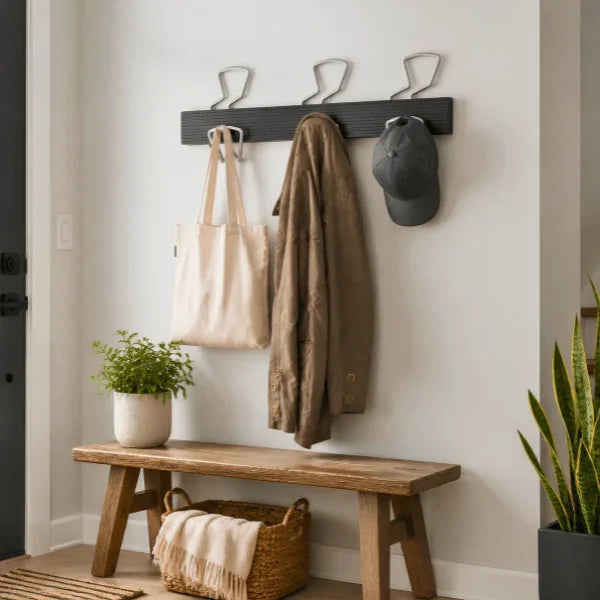 Alba wall coat peg rack holding a tote bag, brown jacket, and grey cap above a wooden bench.
