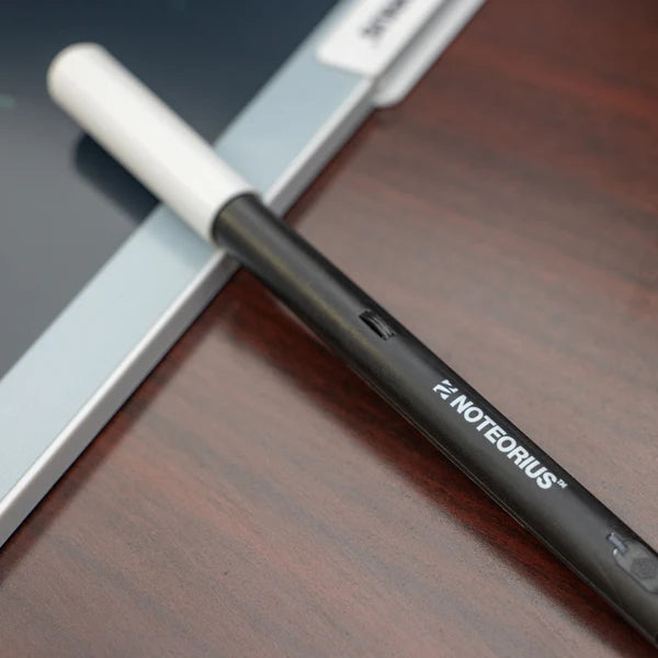 Digital smart notebook pen labeled "Notorius" on a wooden desk near a tablet.