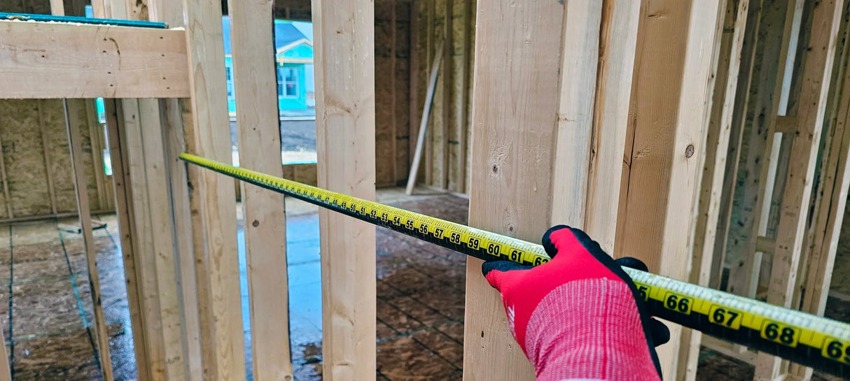 Hand in red glove measuring wooden frame with yellow tape measure during construction