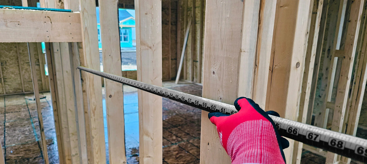 A person wearing red gloves using a Victor ProSpan magnetic measuring tool in wall framing.