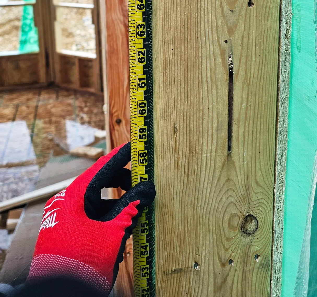 Hand in red glove measuring wooden beam with tape measure during construction