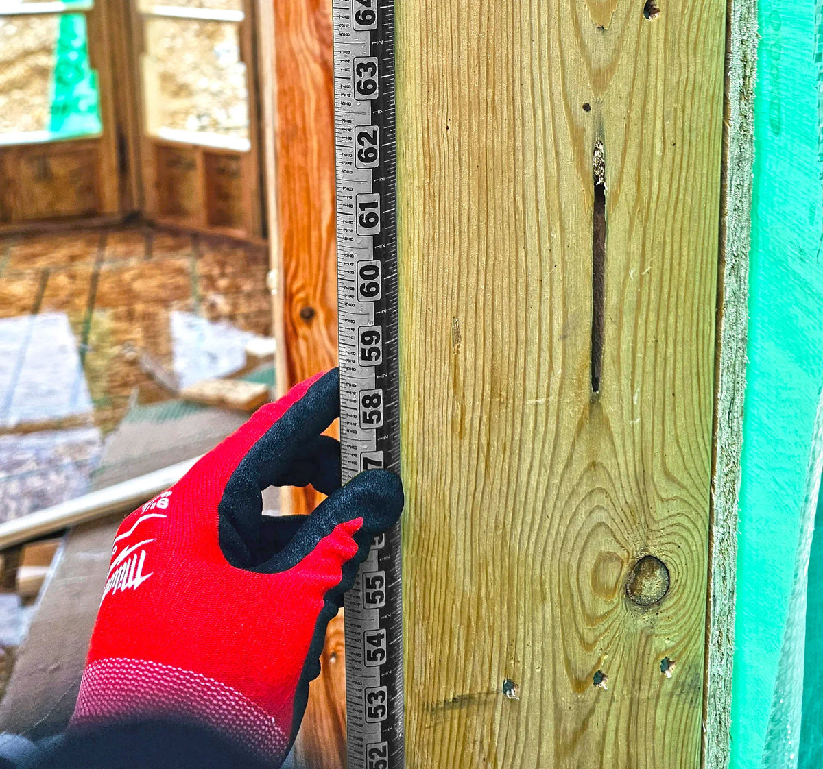 A hand in a red glove using a Victor ProSpan magnetic measuring tool on a wooden beam.