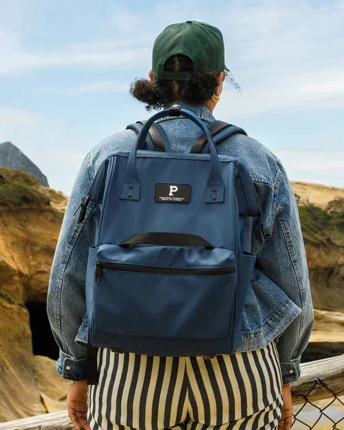 Person wearing navy blue backpack with front pocket, standing outdoors near rocky cliffs