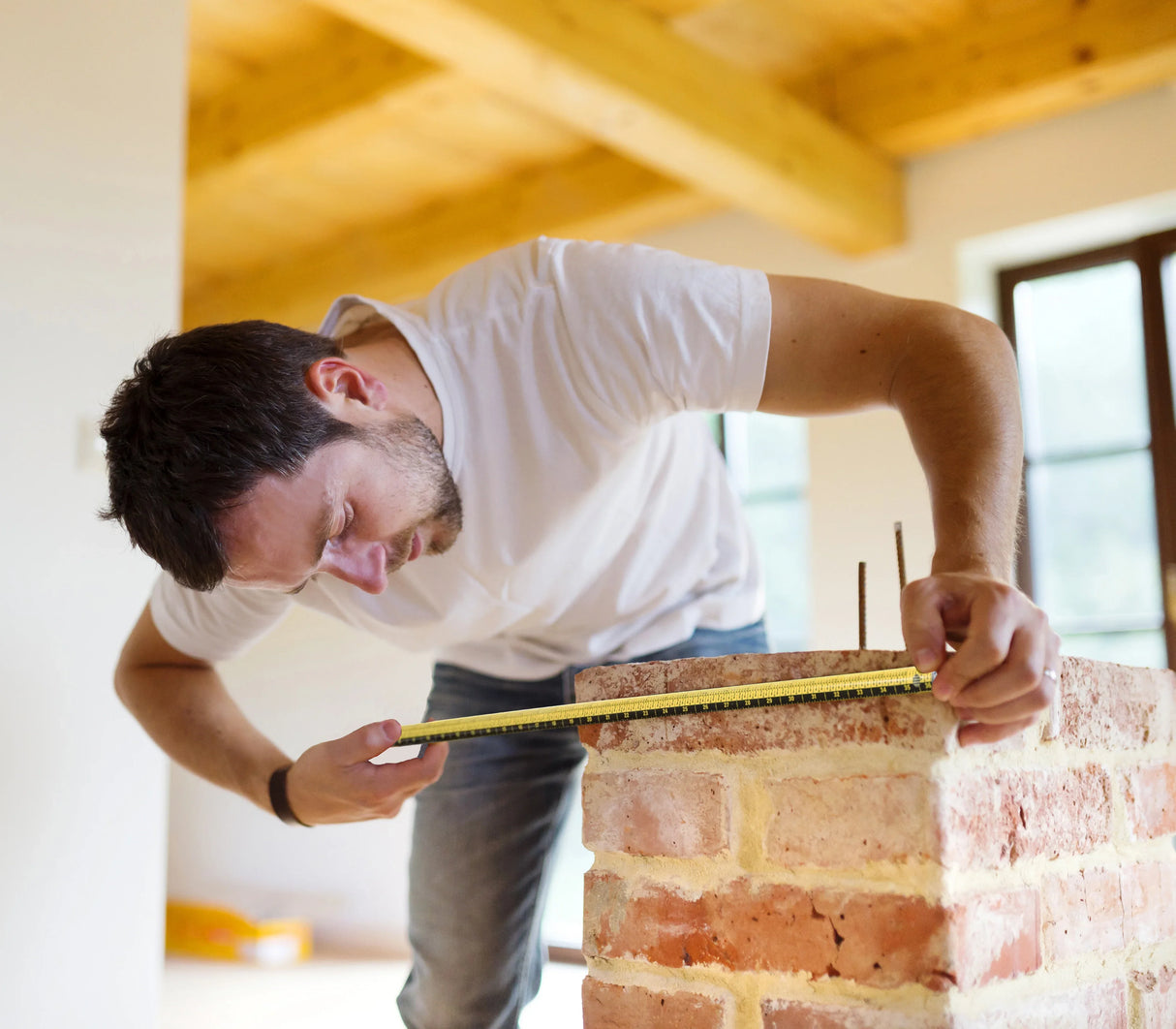 Man measuring a brick wall in a room with wooden beams. He is using a Zip Stick ruler