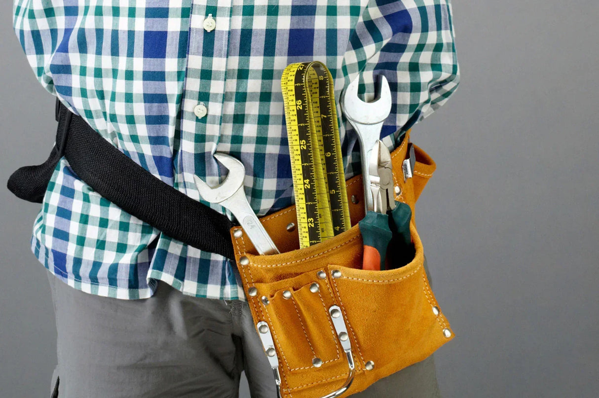 Person wearing plaid shirt with tool belt holding wrench, tape measure, and pliers for DIY projects