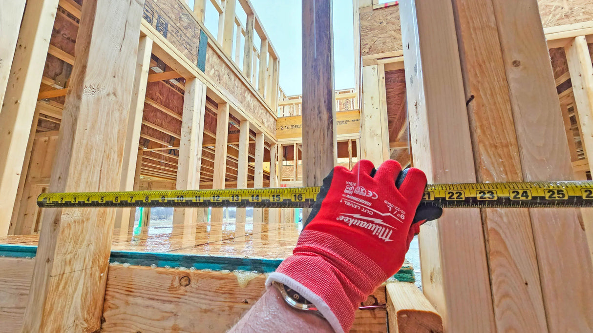 Hand in red glove measuring wooden frame with tape measure at construction site