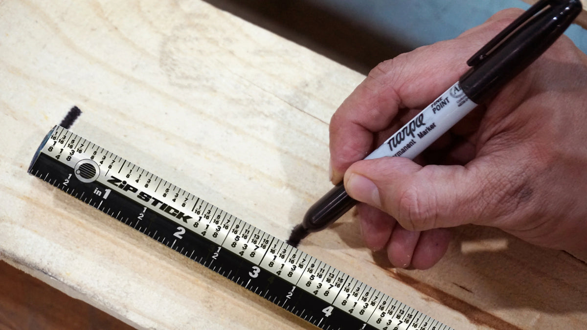 Hand using a marker to mark a measurement on a Victor® Zip Stick magnetic ruler on wood.