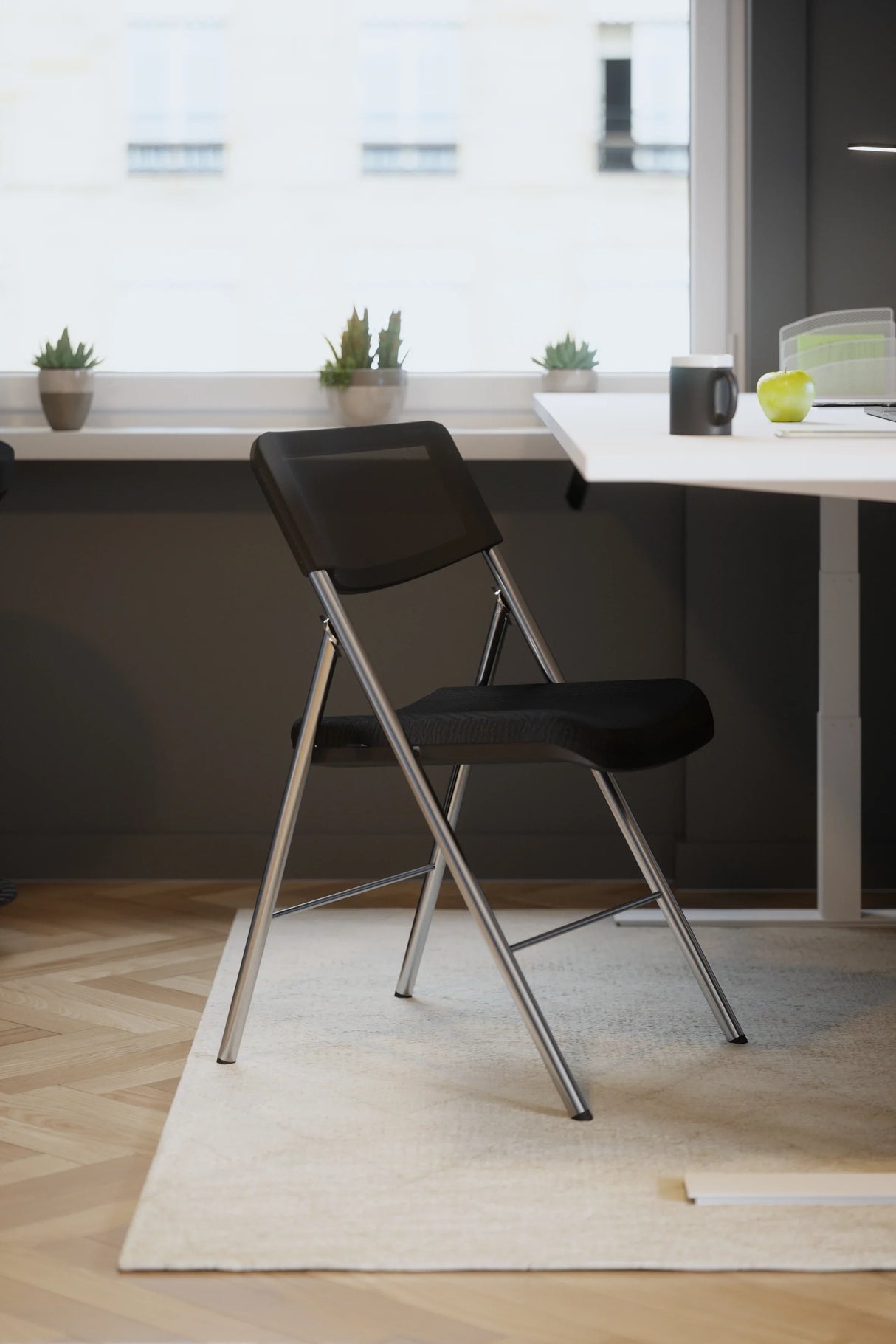 Black mesh folding chair with chrome frame in modern office setting near desk and window