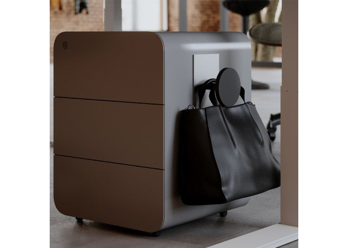 Black magnetic peg hook holding a black bag on a gray office drawer unit in a modern workspace