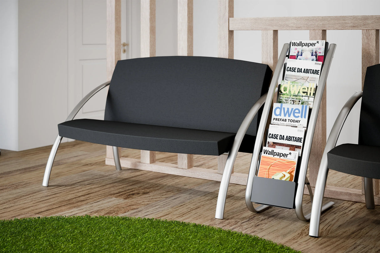Modern black two-seat reception chair with silver legs beside a magazine rack in a waiting area
