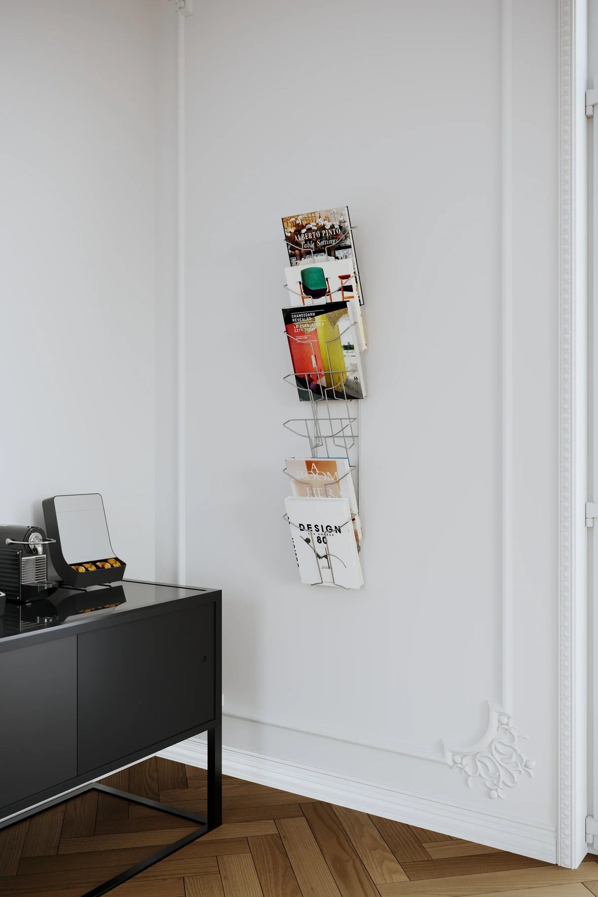 Wall-mounted metal magazine rack holding design books in modern office with black console table