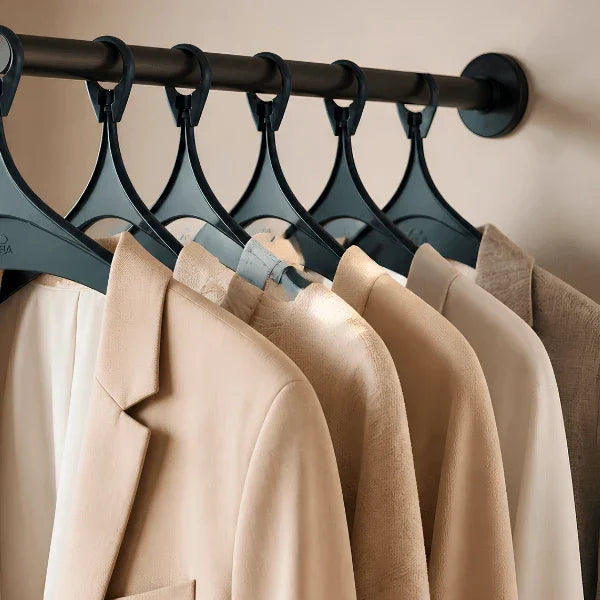 Set of durable black Alba anti-theft plastic clothes hangers holding beige blazers on a rack.
