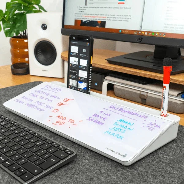 White dry-erase desk board with handwritten tasks, pen holder, and smartphone stand on office desk