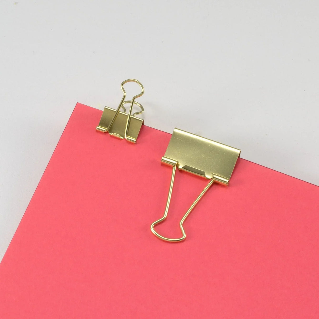 Golden binder clips on pink paper for office organization
